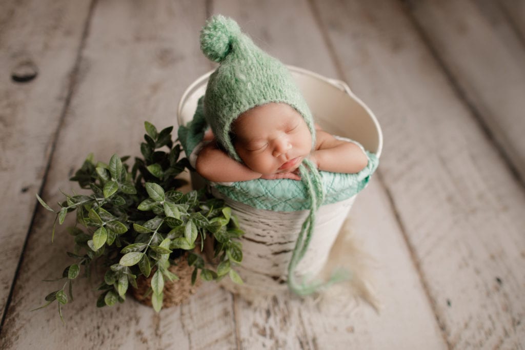 baby girl in green hat in a bucket 