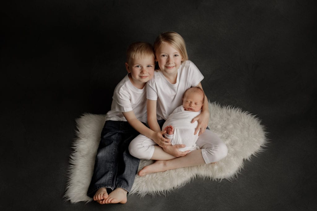 siblings cuddle their newborn baby brother