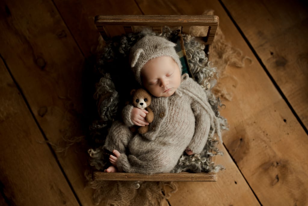 baby boy asleep on miniature bed with teddy bear