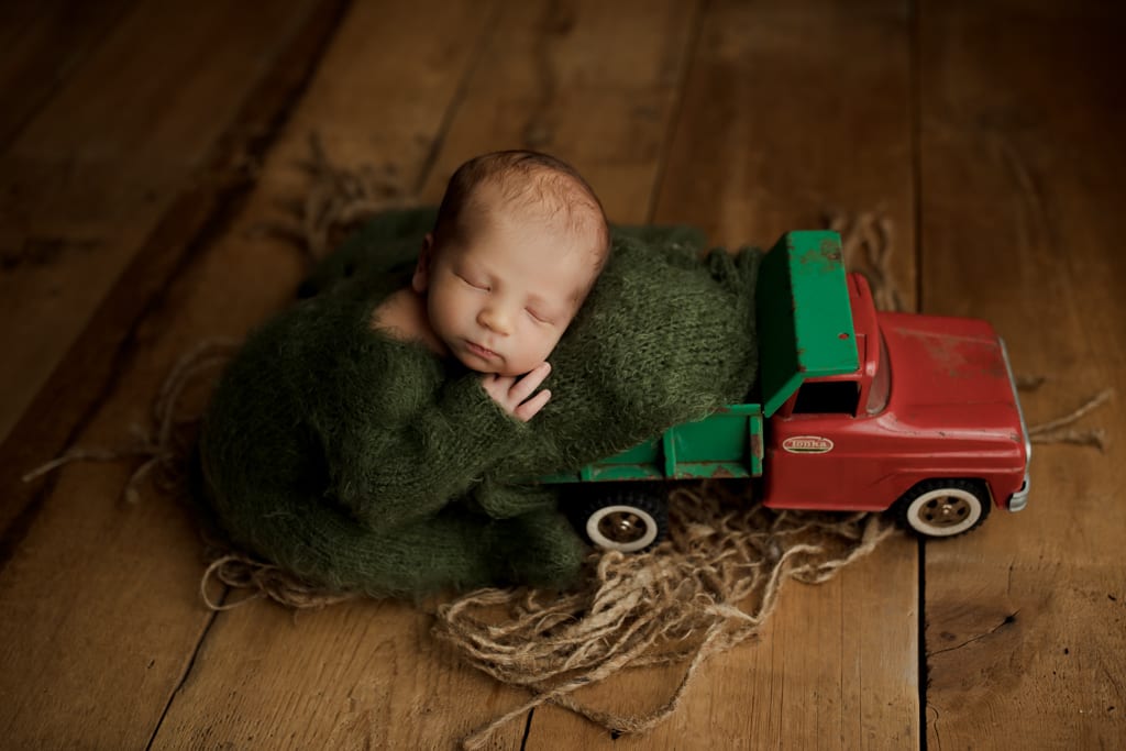 Best newborn photographers near me Chicago, baby in green with model truck toy