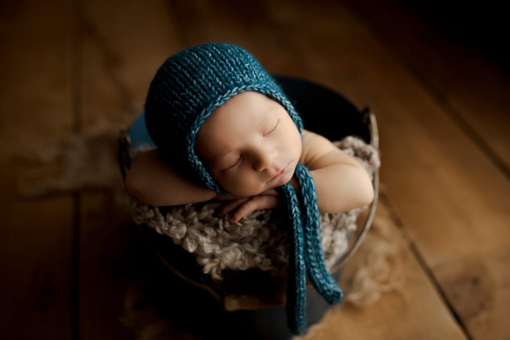 newborn pictures Palatine/Chicago, baby in blue cap sleeping in bucket