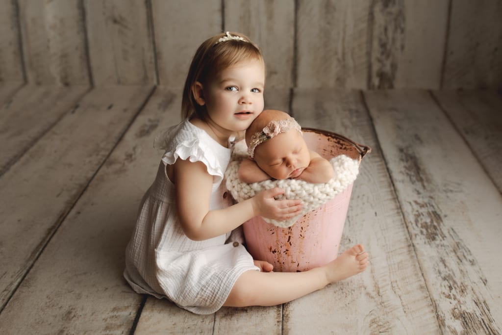 Newborn and sibling photos Chicago, baby girl asleep in bucket with older sister seated next to her