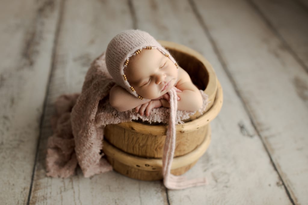 baby girl asleep in bucket with pink beaded cap
