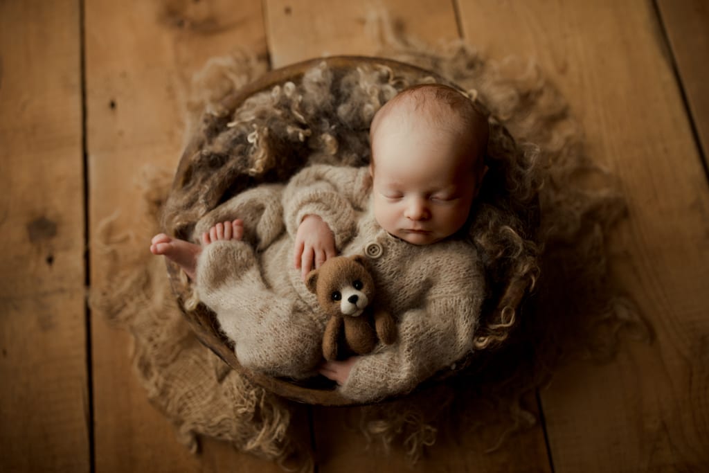 baby boy asleep in basket with tiny teddy bear