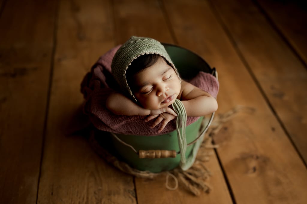 Chicago newborn pictures, infant asleep in green bucket with crocheted cap