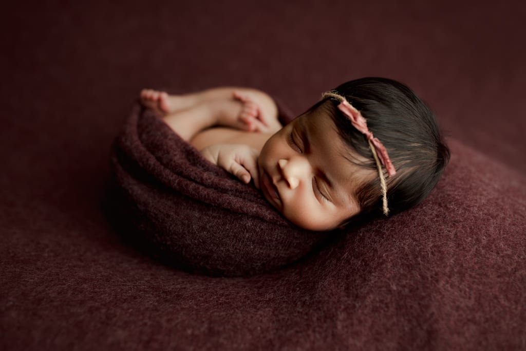 Chicago newborn photoshoot, baby girl bundled on beanbag in plum blanket