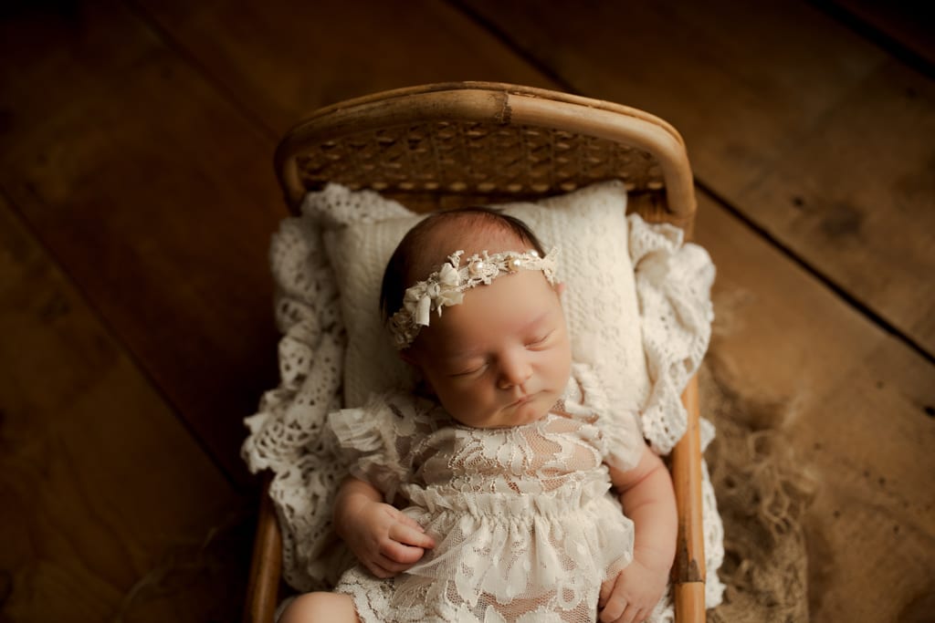 best newborn photographers Chicagoland, baby girl in white lace dress asleep in wooden cradle