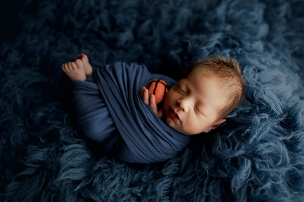 newborn in blue swaddle with basketball prop