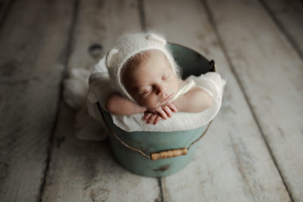 Baby boy asleep in bucket wearing teddy bear cap