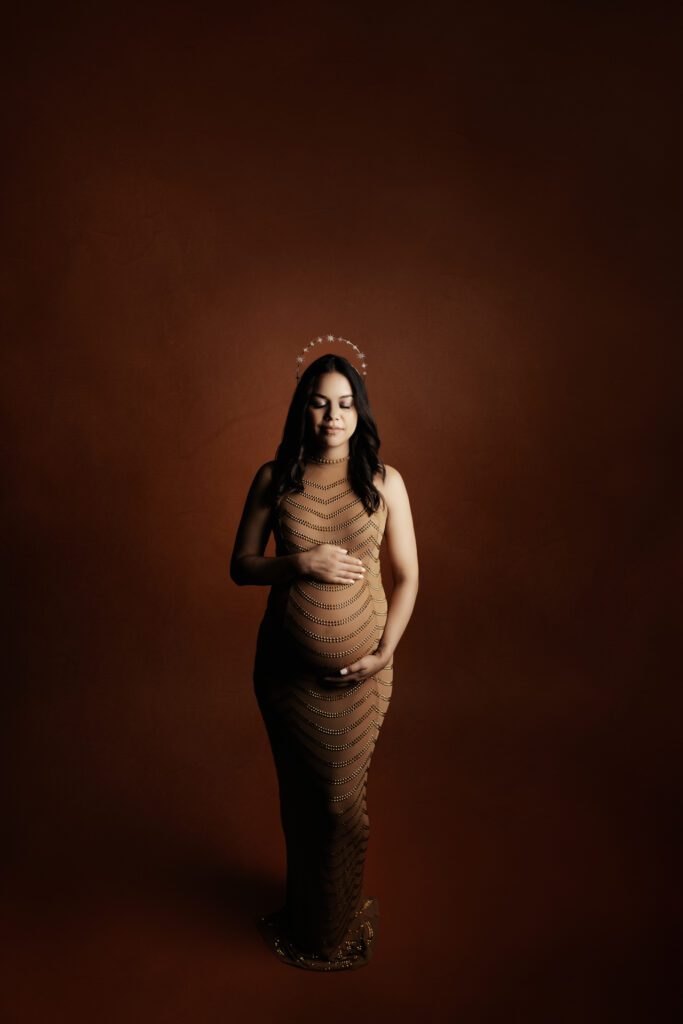Pregnant woman in gold dress with her hands resting on her belly