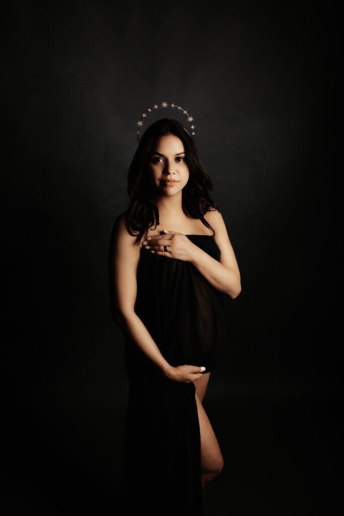 Woman in loose black dress with silver crown of stars posing during Chicago maternity photoshoot