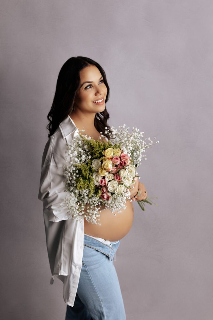 Woman in jeans and open shirt holding bouquet during Chicago maternity photoshoot