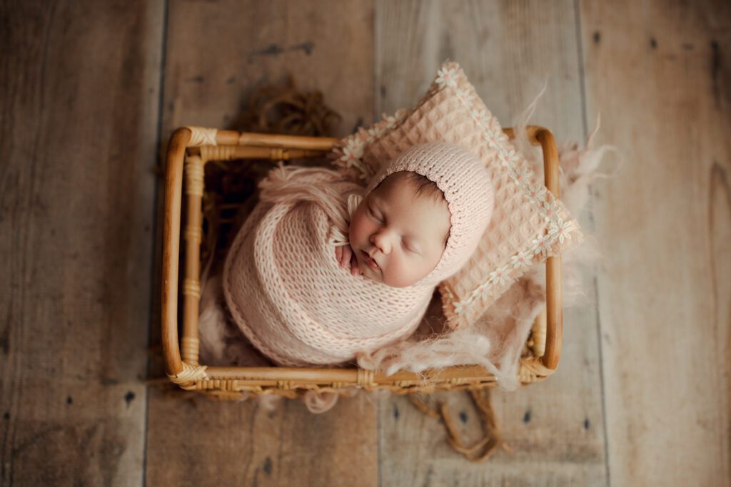 Baby girl bundled in soft pink lying in a wicker basket