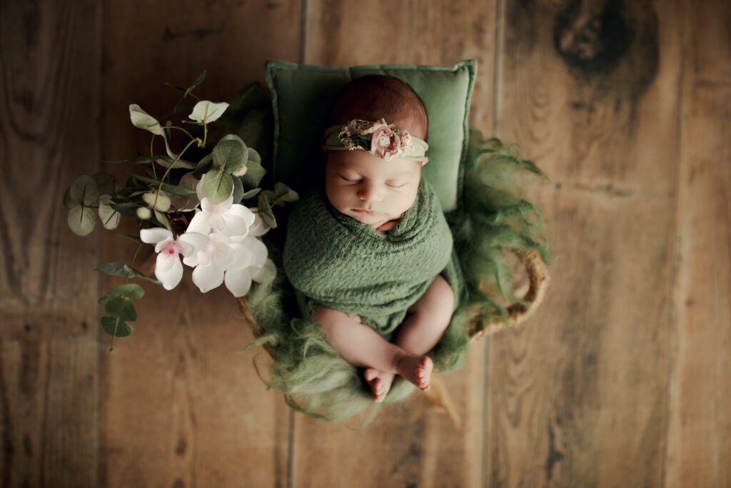 Infant girl in green wrap with flowers by Chicagoland newborn photographer Agata Brannon