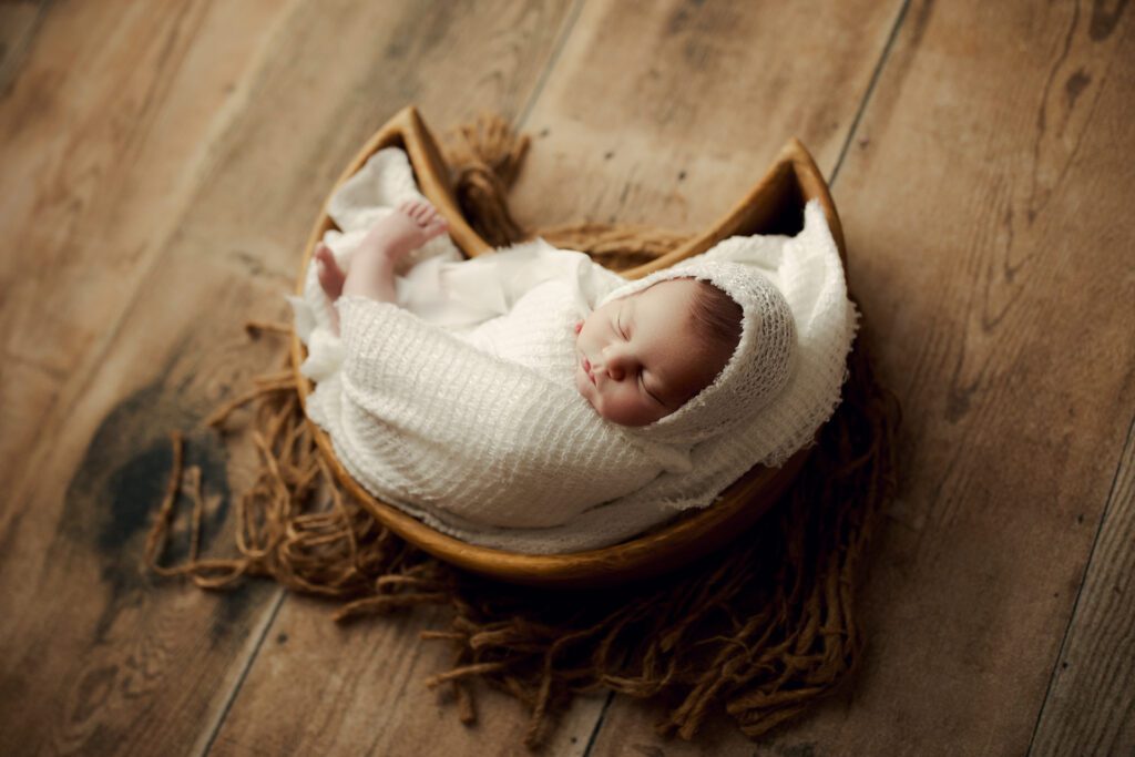 Newborn girl in white swaddle lying in moon basket