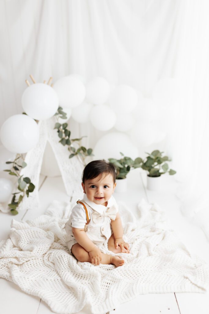 Baby boy surrounded by white balloons during milestone sitter session