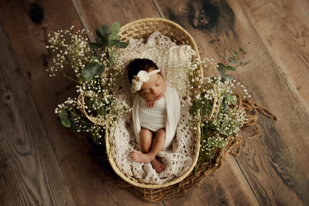 Infant girl swaddled in basket surrounded by baby's breath flowers