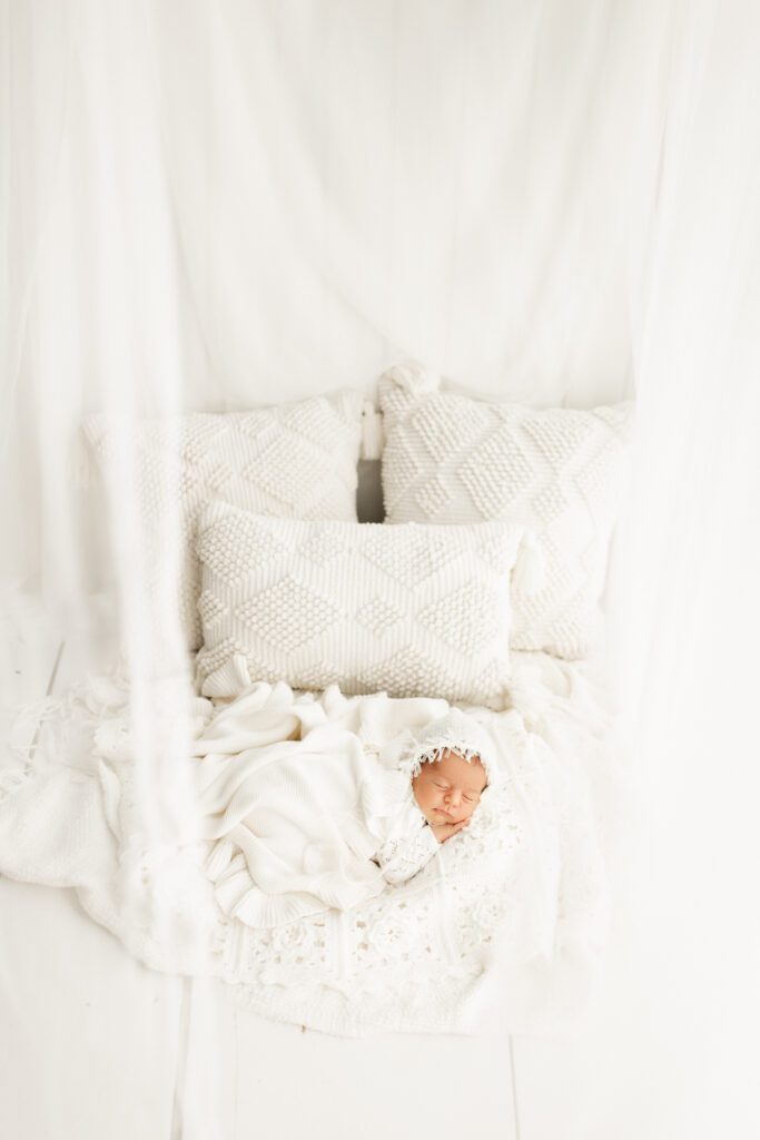 Baby curled up in the middle of white bed with curtains