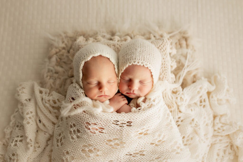 Newborn twin girls in white knitted wrap and hats