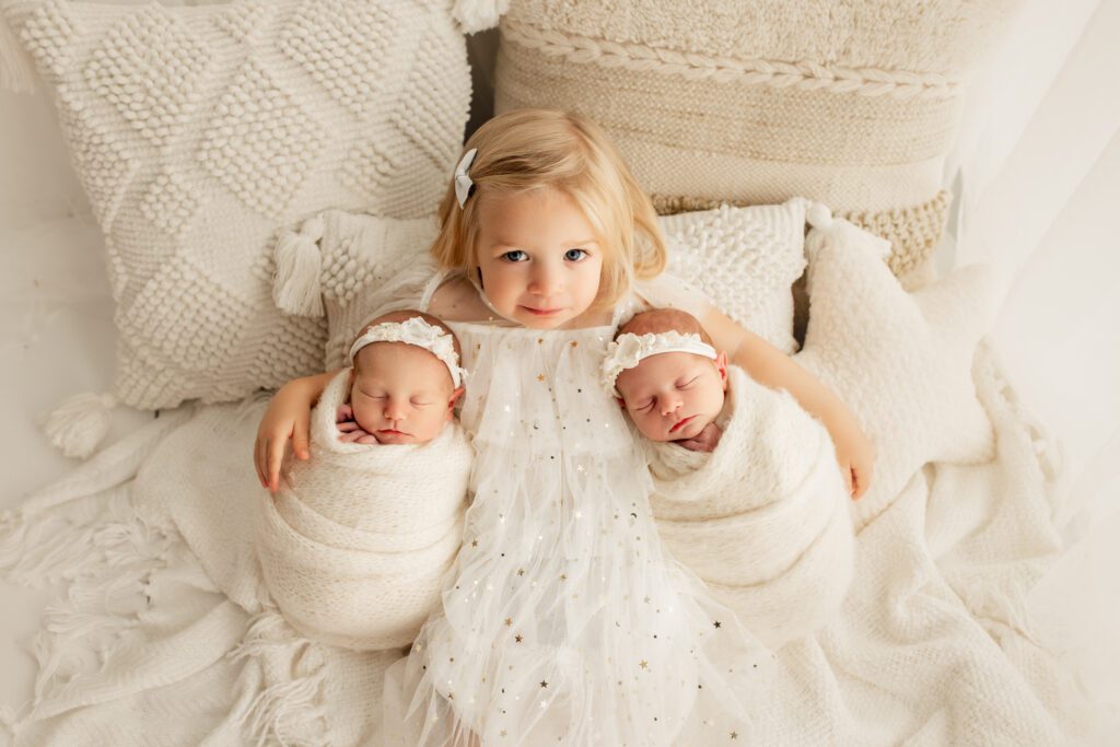 Big sister with her arms around new twin siblings