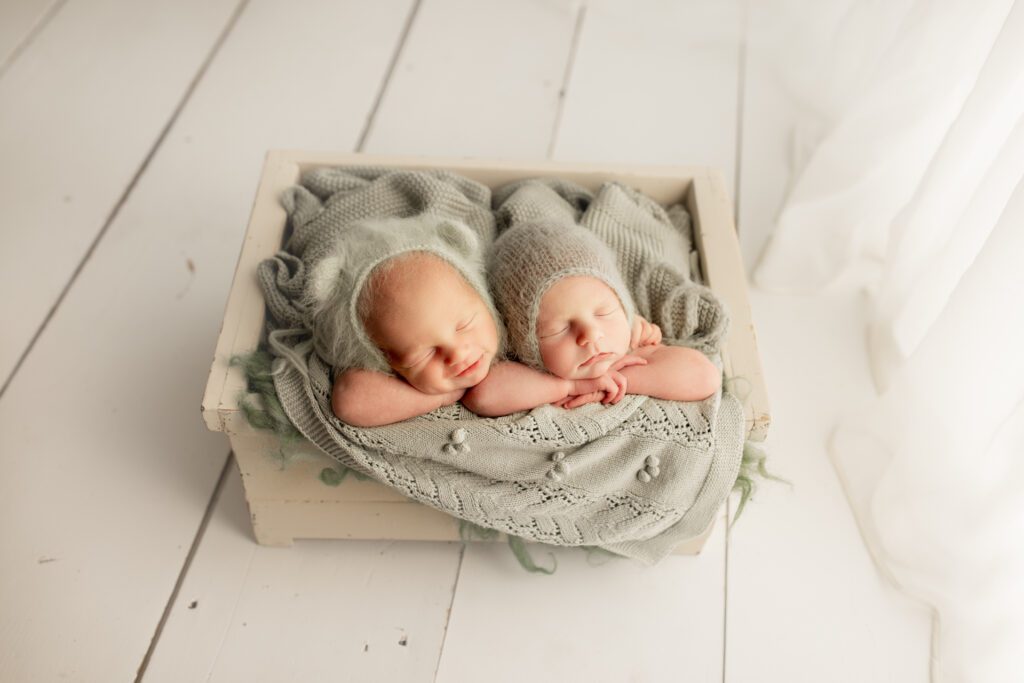 Newborn twins curled up together in gray blanket