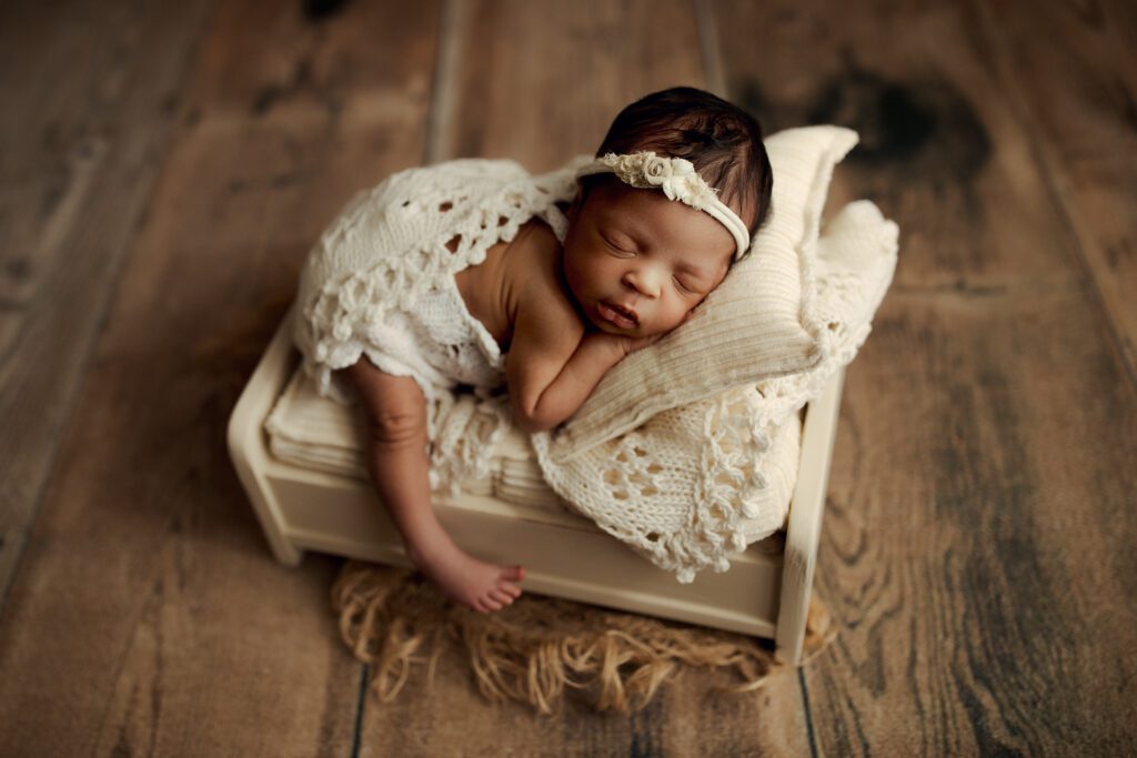 Newborn African American girl asleep on miniature bed prop