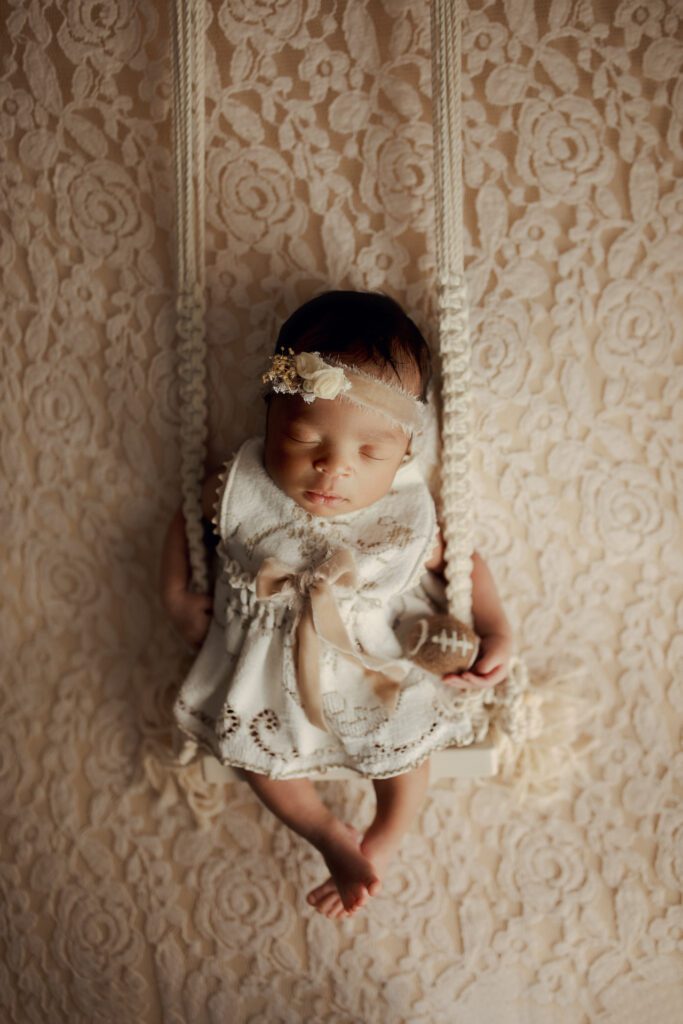 Newborn girl asleep on swing holding tiny football