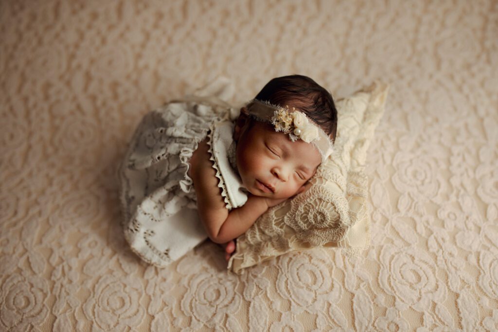 Newborn girl curled up on lacy pillow, by Chicago newborn photographer