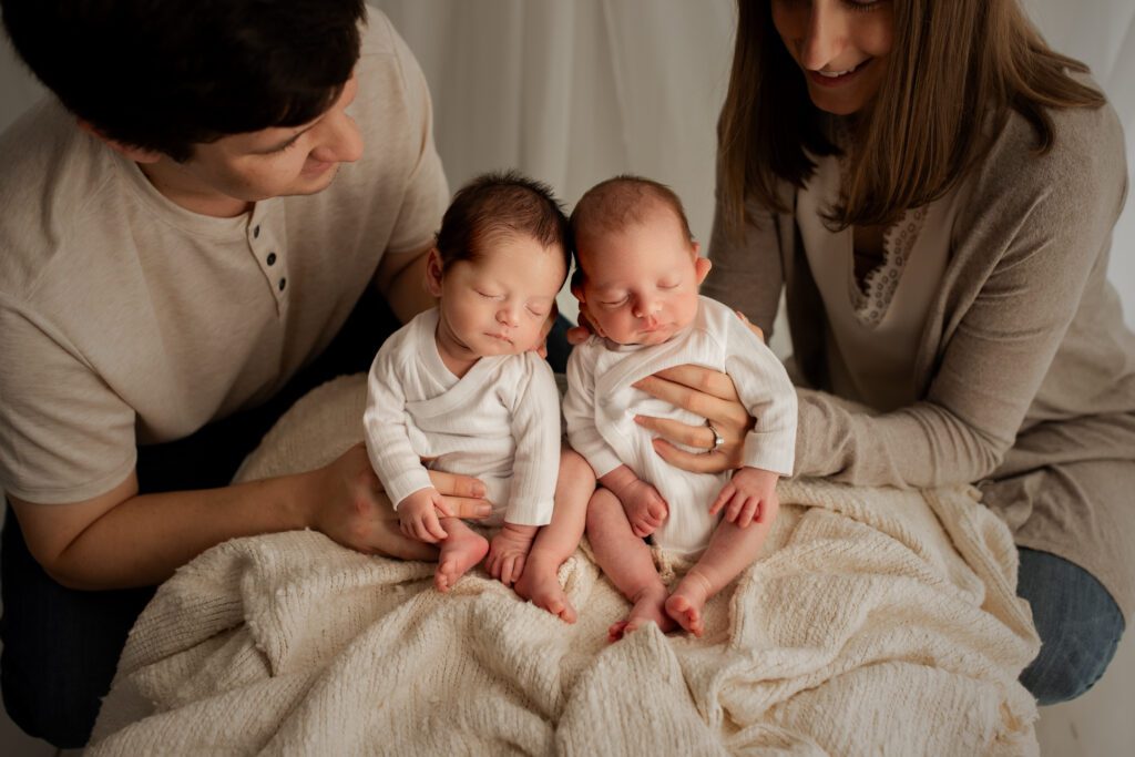 Mother and father holding newborn twin boys on their laps in photo studio near Chicago, Illinois