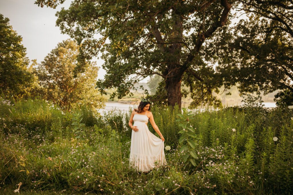 Woman in white maternity dress standing under trees in a wooded area near Chicago