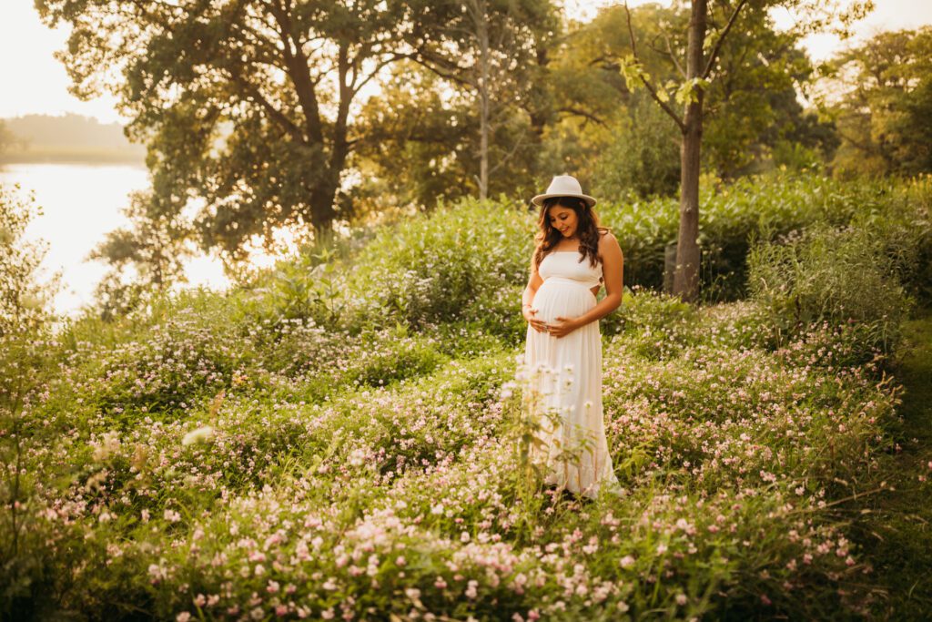 Outdoor maternity portrait, woman in white dress standing among blossoms