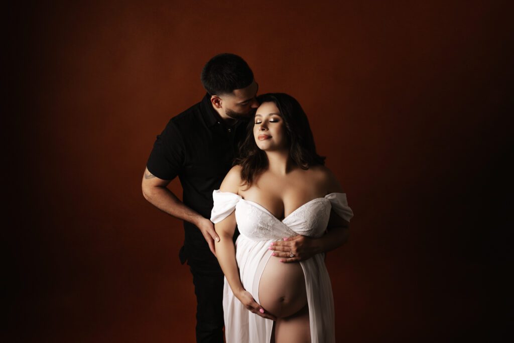 Husband kissing pregnant wife during maternity photoshoot in studio near Chicago