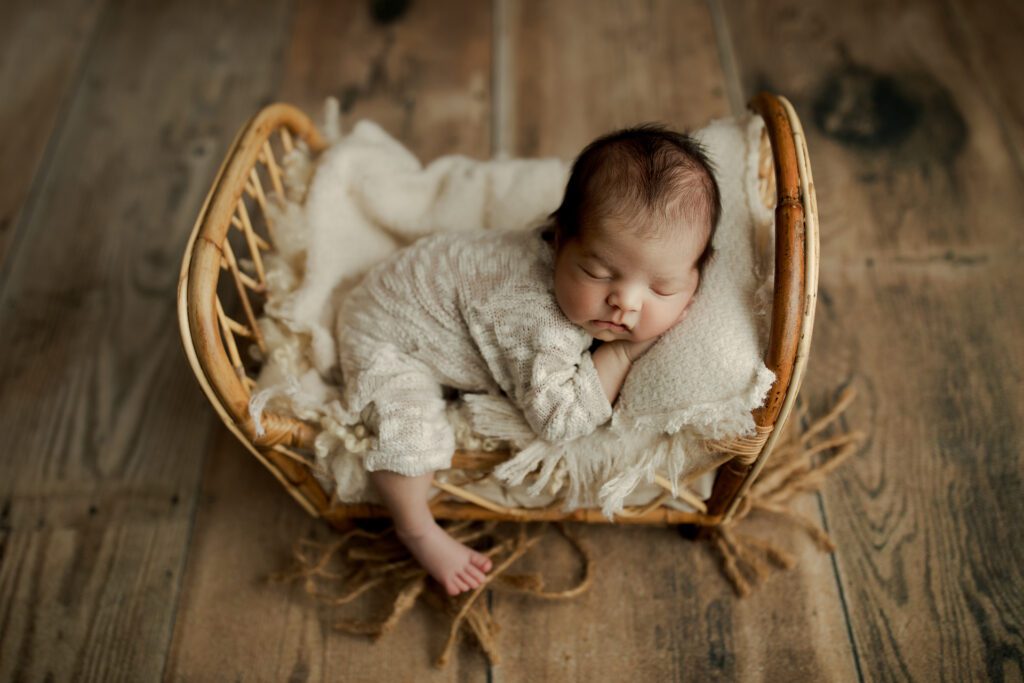 Newborn boy sleep on miniature wicker bed in Long Grove photo studio