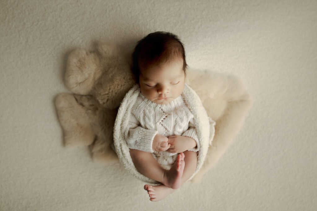 Infant boy in white wrap swaddled on faux fur prop