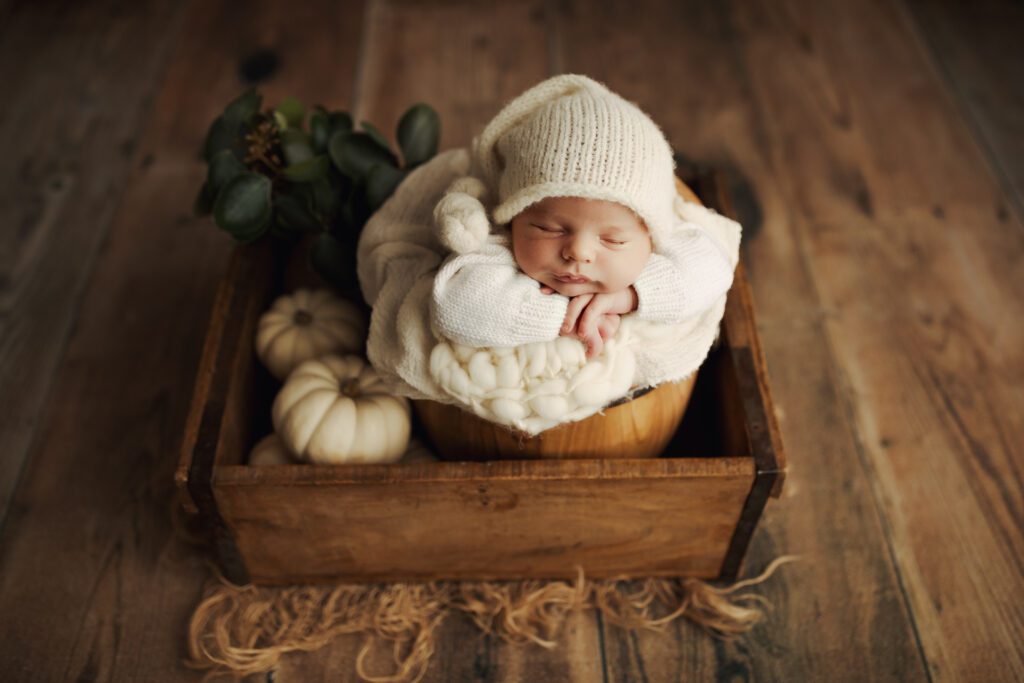 Portrait of Chicago newborn in white knit hat asleep in wooden box with cream-colored pumpkins