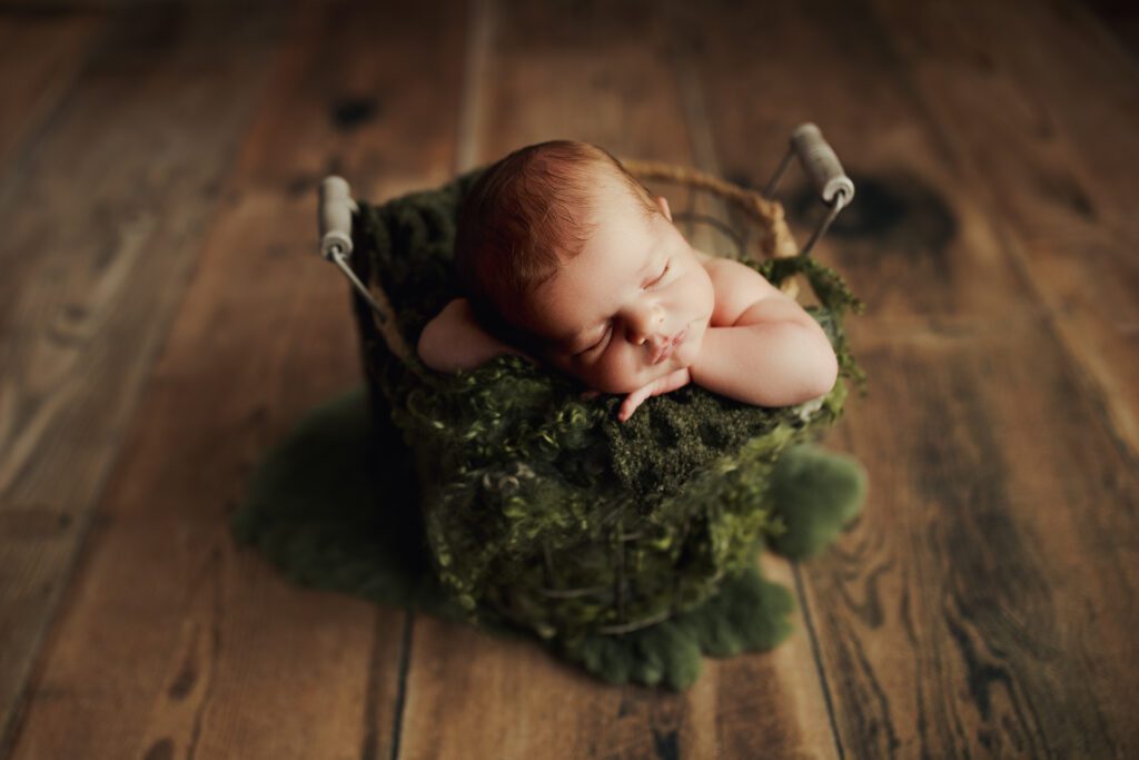 Baby boy asleep in rustic bucket with forest green blankets