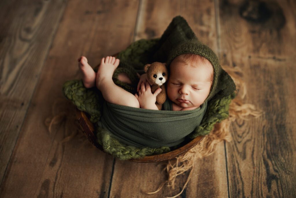 Baby boy in green swaddle cuddling teddy bear