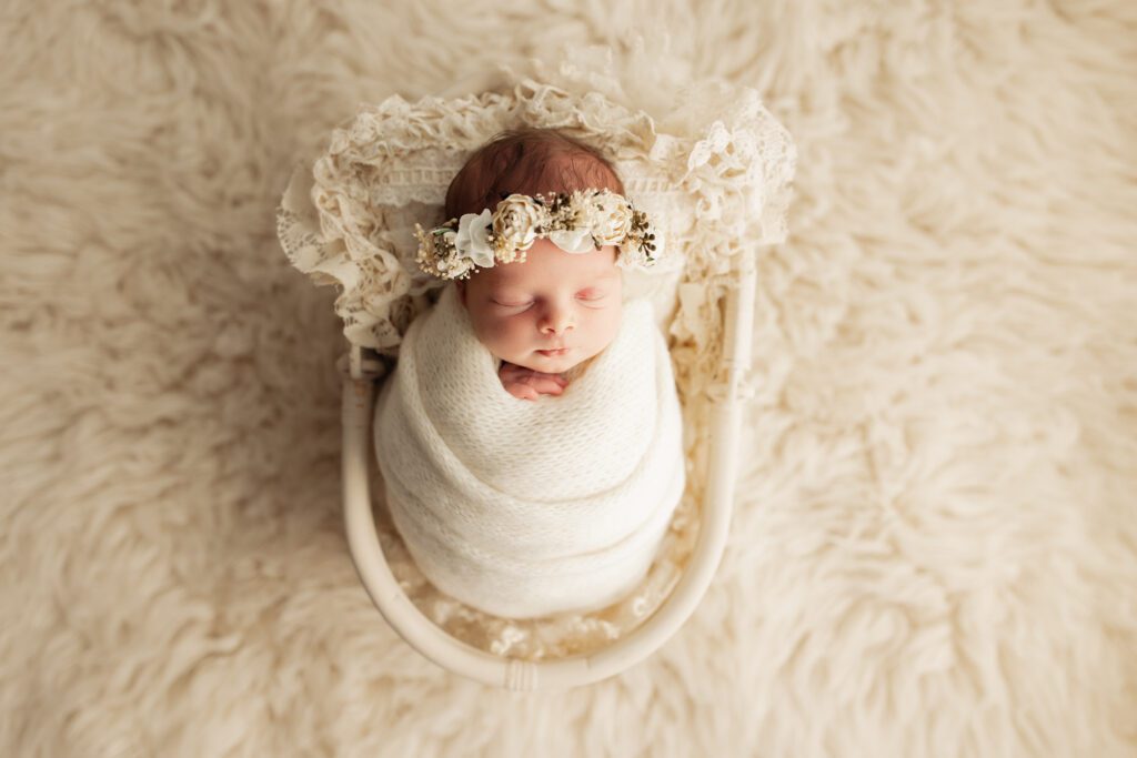 Baby girl wearing white flower crown asleep in basket in photo studio near Chicago