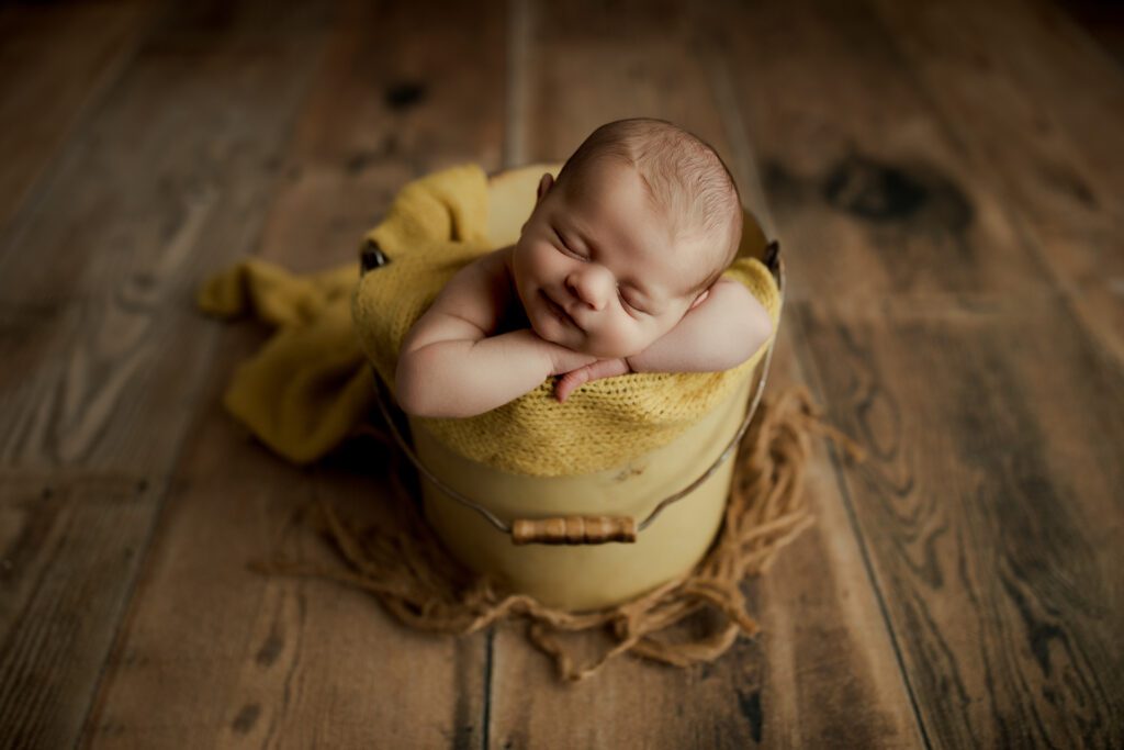 Smiling infant boy asleep in yellow bucket in photo studio near Chicago