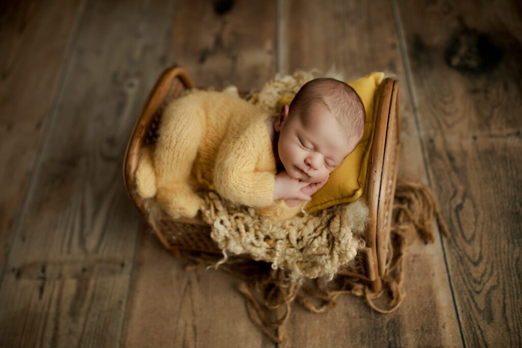 Newborn boy in yellow asleep on miniature bed