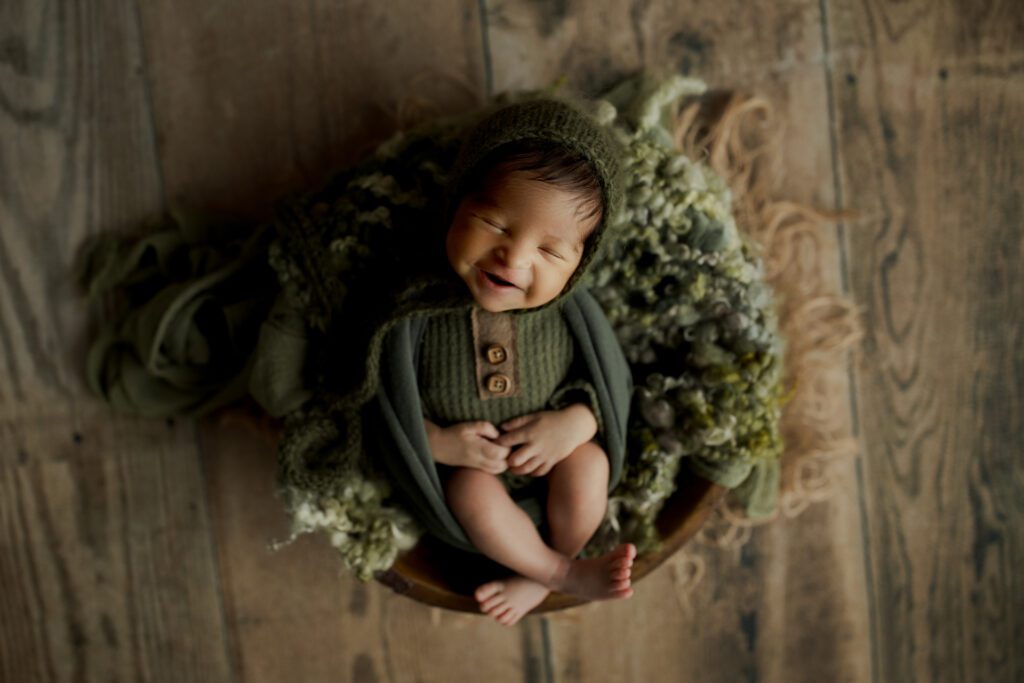 Newborn boy in forest green smiling in his sleep during photoshoot