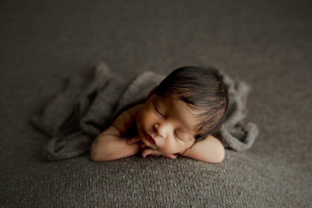 Baby asleep with chin on hands against gray backdrop in Chicagoland photo studio