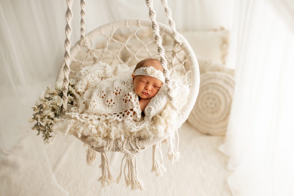 Infant girl asleep in white swing near window