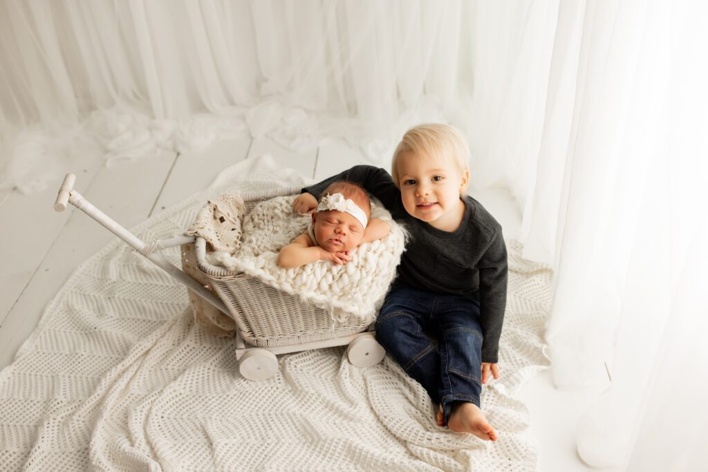 Toddler boy seated next to sleeping newborn sister in Chicagoland photo studio