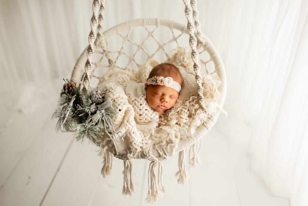 Baby girl asleep in white swing with flocked pine cones and greenery