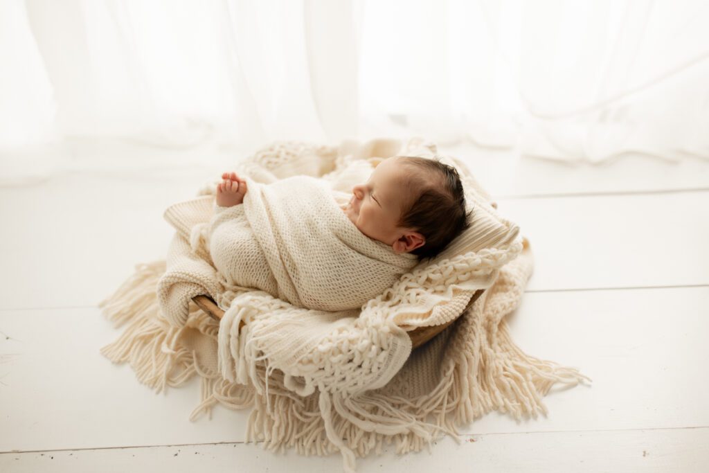 Swaddled newborn in cushioned basket asleep by window of photography studio near Vernon Hills Illinois