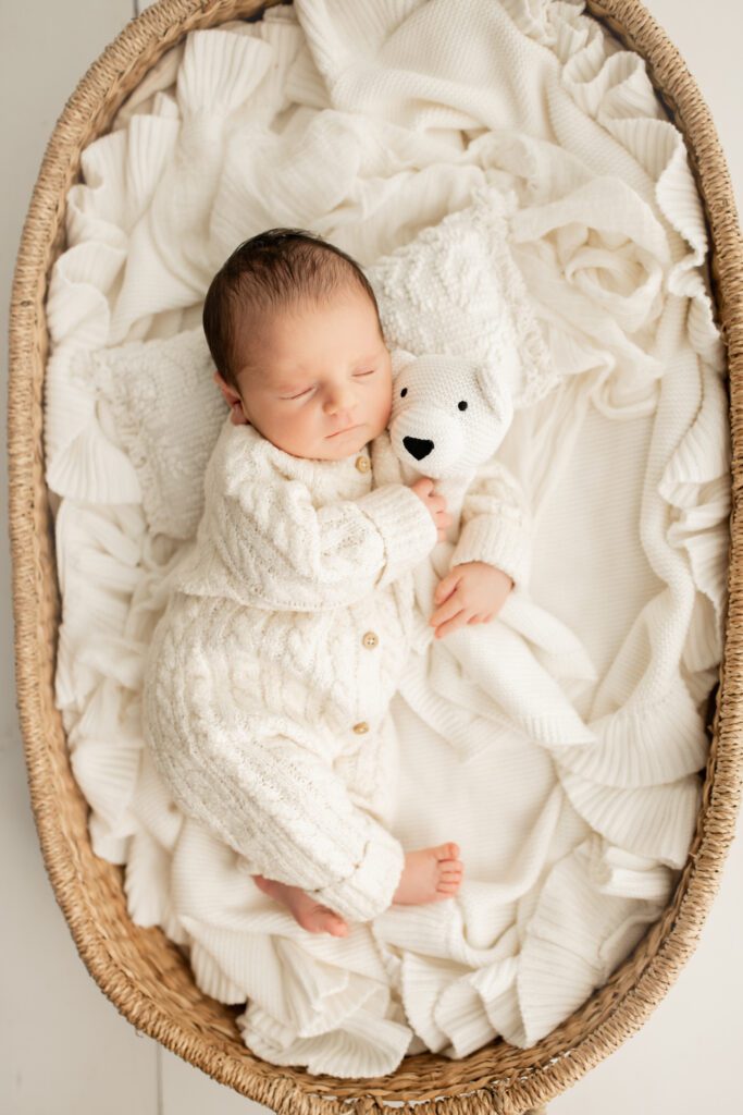 Newborn baby asleep in basket cuddling white teddy bear