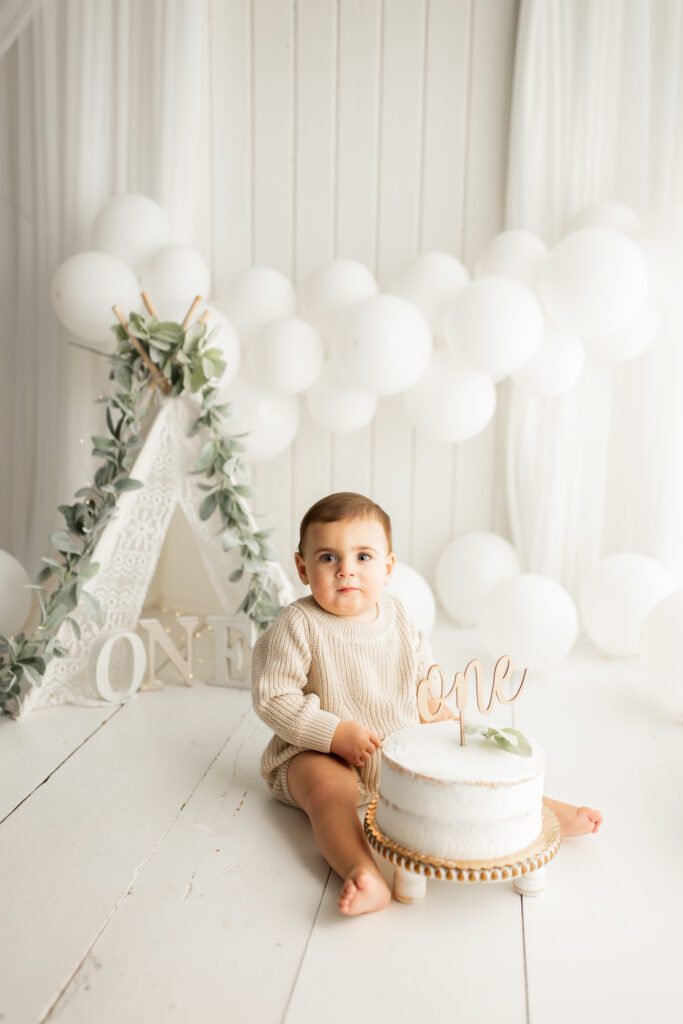 Baby in white studio setup with first birthday cake