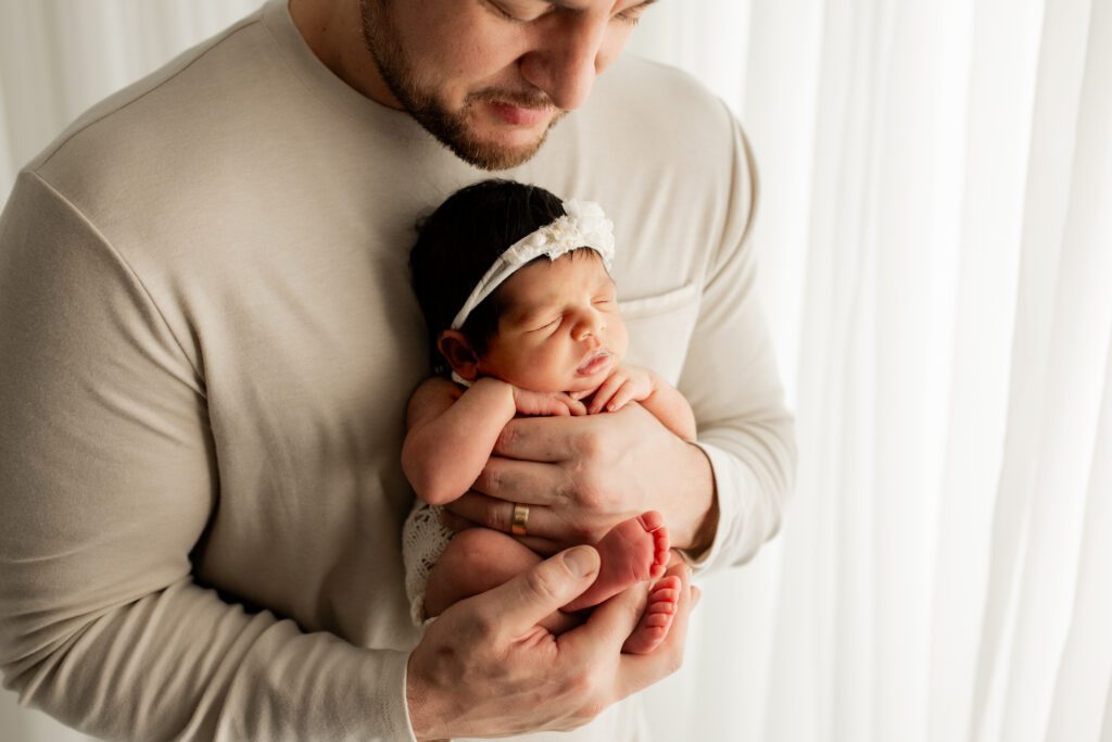 Daddy holding new baby girl near window in Long Grove photo studio
