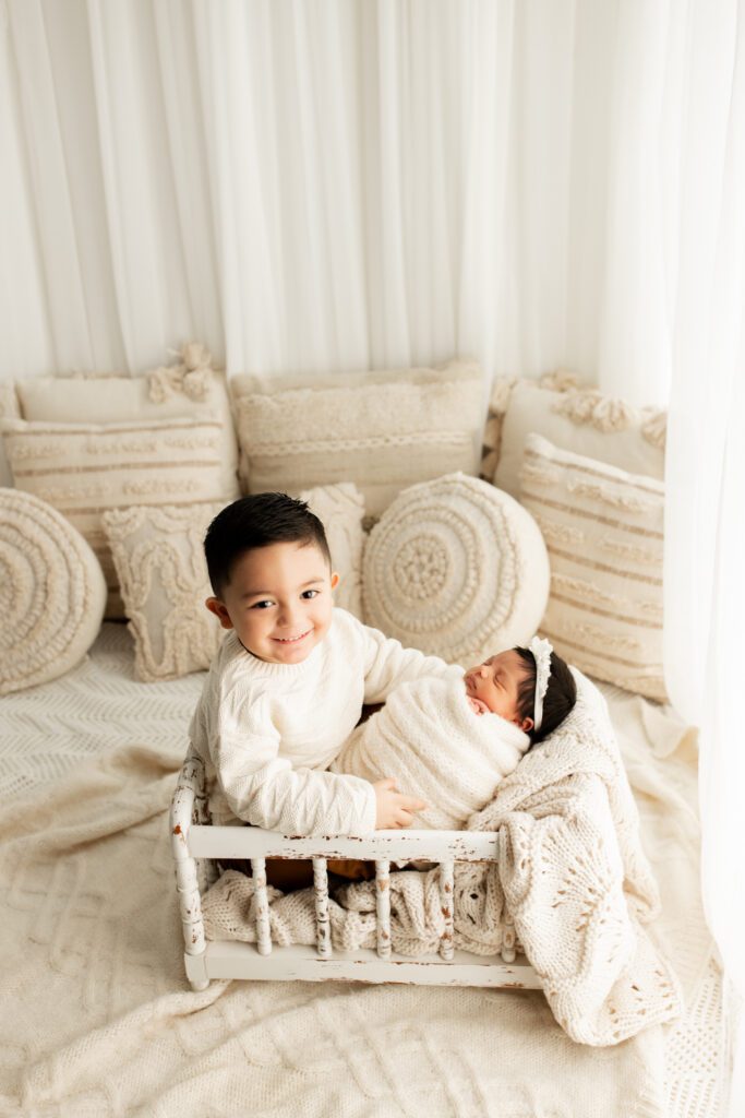 Toddler brother in shabby chic white crib holding new baby sister